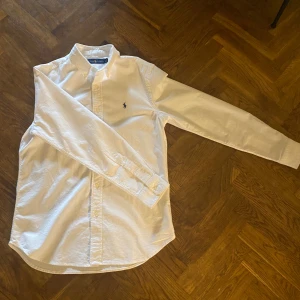 Vit skjorta från Ralph Lauren - Klassisk vit skjorta från Ralph Lauren med button-down krage och broderad marinblå logga på bröstet. Tröjan passar nog M  bättre än S då den e ganska stor i storleken. Säljs då den inte passar mig. Priset går absolut att diskuteras!!