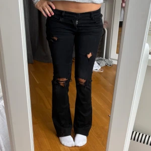 Svarta bootcut jeans från J Brand - Säljer ett par svarta jeans från J Brand med bootcut-modell och slitna detaljer på knäna och låren. Jeansen har låg midja och är i storlek W25.💖💖