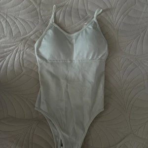 Beige ribbad body med smala axelband - Snygg beige body i storlek XS med smala axelband och ribbad struktur. Bodyfirming. Tillverkad i stretchigt material för skön passform.