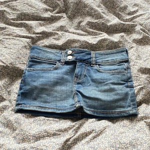 Blå jeanskjol med dubbla knappar - Snygg blå jeanskjol i kort modell med dubbla knappar framtill och klassiska fickor både fram och bak. Perfekt för dig som gillar en avslappnad och trendig stil. Kjolen har bälteshällor och är lätt att matcha med allt.