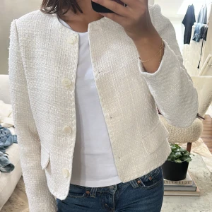 Vit kavaj i tweed med knappar - Säljer en stilren vit kavaj i tweed med stora knappar framtill och två fickor. 