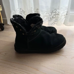 Svarta ÄKTA UGG boots i mocka - Svarta UGG boots med mjukt foder och snörningsdetalj upptill. Skorna är i mocka och har en platt sula samt rund tå. Perfekta för kalla dagar med sin mysiga insida och klassiska UGG-look. Nypris 1.800kr