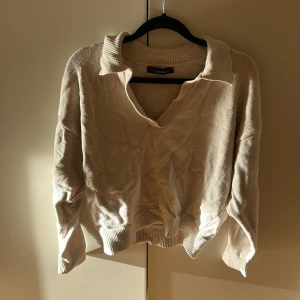 Beige stickad tröja från Dilvin - Beige stickad tröja från Dilvin med krage och v-ringning. Tröjan har långa ärmar och ribbade muddar vid ärmslut och nederkant. Perfekt för lager-på-lager och chill dagar. Snygg och enkel att matcha med jeans eller kjol.