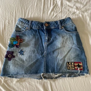 Jeanskjol med broderier från Lexington - Jeanskjol från Lexington med broderade detaljer och patchar, bland annat blommor och stjärna. Stl XXS, insytt. Fraktar gärna tillsammns med andra varor.