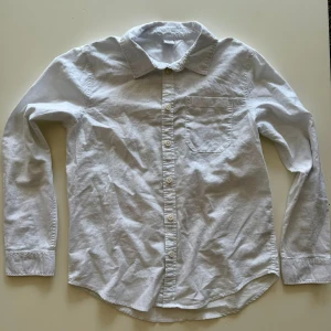 Vit klassisk skjorta med ficka - Vit skjorta i bomull med klassisk krage, lång ärm och bröstficka. Skjortan har knappar hela vägen framtill och en enkel, stilren look som passar till det mesta. Perfekt för dig som gillar en clean och tidlös stil.