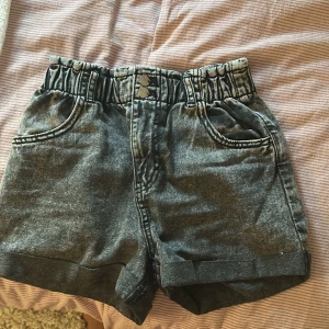 Grå jeansshorts från H&M med resår - Snygga grå jeansshorts från H&M med resår. Shortsen har två knappar framtill, fickor både fram och bak samt uppvikta benslut.