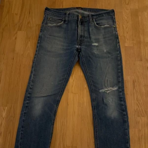 Blå Lee ”Luke”  jeans med slitningar - Snygga blå jeans från Lee ”Luke” med klassisk femficksdesign och slitna detaljer på låret och knät. Jeansen har en rak passform och är tillverkade i mjukt denimtyg. Perfekta för en avslappnad streetstil och passar till det mesta i garderoben.