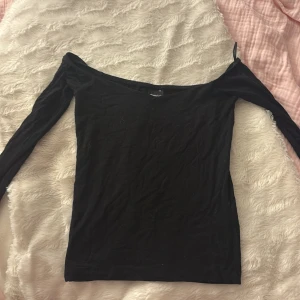 Svart offshoulder topp Gina Tricot XS - Svart långärmad offshoulder topp från Gina Tricot i storlek XS. Toppens smala passform och vida halsringning ger en snygg och stilren look. Perfekt att matcha med jeans eller kjol för en trendig outfit.