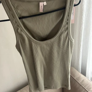 Ribbad khakigrön linnetopp från Nelly - Ribbad khakigrön topp från Nelly. Toppen har rund halsringning, ärmlös design och är tillverkad i mjuk bomullsmix. Perfekt att styla med jeans eller kjol för en enkel och snygg look.