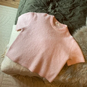 Ljusrosa stickad tröja Gina Tricot - Supermjuk ljusrosa stickad tröja från Gina Tricot i ullblandning. Tröjan har korta ärmar, rund halsringning och en lite boxig, loose passform. Perfekt för lager-på-lager och ger en söt vibe till din outfit.