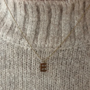 Guldhalsband med bokstav E från Edblad - Snyggt halsband i guld från Edblad med ett  E-hänge. Kedjan är tunn. Liten rund bricka vid låset med Edblad logga. Passar dig som vill ha något enkelt men ändå unikt.