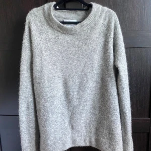 Grå stickad tröja från Samsøe Samsøe - Mysig gråmelerad stickad tröja från Samsøe Samsøe i storlek S. Tröjan har en rund halsringning, lång ärm och en fluffig, mjuk känsla. Perfekt nu till hösten.