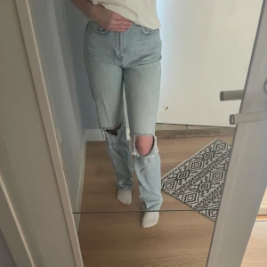 Ljusblå jeans från Gina Tricot - Ljusblå jeans från Gina med raka ben och stora slitningar över båda knäna. Hög midja och klassisk femficksmodell. Bara att höra av sig om man undrar något💕
