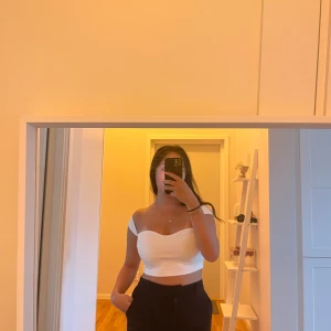 Vit croppad offshoulder topp - Säljer en vit croppad topp med offshoulder-design och korta ärmar. Toppen har en snygg, hjärtformad halsringning och är figurnära. Materialet är ribbad bomull som känns mjukt mot huden och ger en fräsch look.