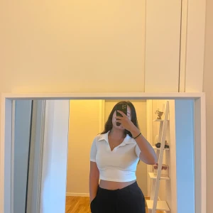 Vit croppad polotopp med krage - Säljer en vit croppad polotopp med korta ärmar och snygg krage. Toppen har en v-ringad öppning framtill och är gjord i ett ribbat material som sitter bekvämt och snyggt. Perfekt för dig som gillar stilrena och trendiga plagg.