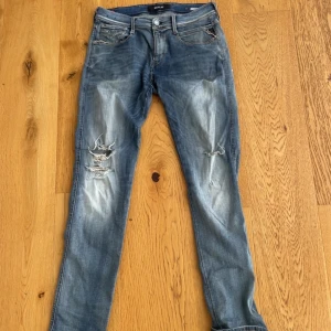 Replay Anbass blå slitna jeans - Säljer ett par Replay Anbass jeans i blå tvätt med slitningar och hål på benen. Klassisk femficksmodell med snygga detaljer på bakfickorna och bekväm passform. Perfekta för dig som gillar en avslappnad och trendig look.