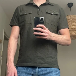 Oscar Jacobson - Snygg mörkgrön t-shirt från Oscar Jacobson med krage och knappar framtill. Två bröstfickor med lock och knappdetaljer ger en cool look. Perfekt till jeans eller shorts för en avslappnad stil.