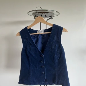 Mörkblå manchesterväst från Cappuccini - Supersnygg mörkblå väst i manchester från Cappuccini med broderade blommor framtill och fyra knappar. Västen har en klassisk v-ringning och är fodrad på insidan. Köparen står för frakt 💞