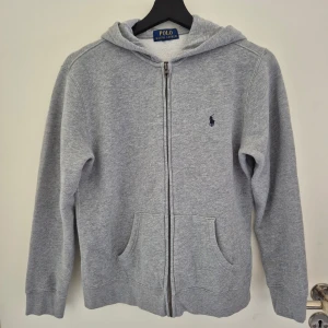 Grå hoodie från Ralph Lauren - Säljer en grå zip up från Ralph Lauren med dragkedja och huva. Klassisk broderad logga på bröstet, känguruficka framtill och mjukt material i bomull. Köp på kidsbrandstore för 1250kr. Pris kan diskuteras. Strl L (14-16)