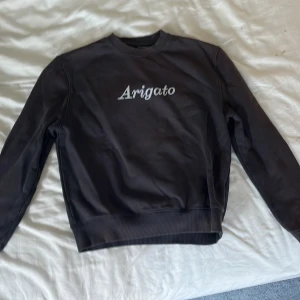 Svart sweatshirt från Axel Arigato - Snygg svart sweatshirt från Axel Arigato med vit Arigato-text på bröstet. Tröjan har rund halsringning, ribbade muddar och är tillverkad i mjuk bomull. Perfekt för en clean och stilren look.