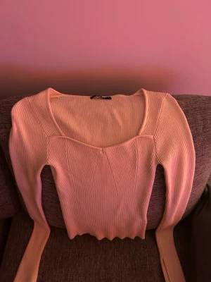 Ljusbeige ribbad långärmad topp - Supersnygg ljusbeige ribbad topp med lång ärm och unik v-ringad skärning. Toppen har en croppad passform och är tillverkad i mjuk stretchig bomullsmix. Perfekt att styla med jeans eller kjol för en trendig look.