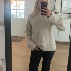 Beige stickad tröja med krage - Mysig beige stickad tröja med gråa ribbade muddar vid ärmslut, hals och nederkant. Tröjan har en högre hals och en relaxed, loose passform. Perfekt för lager på lager under kyliga dagar. Säljer då den är för stor, aldrig använt!