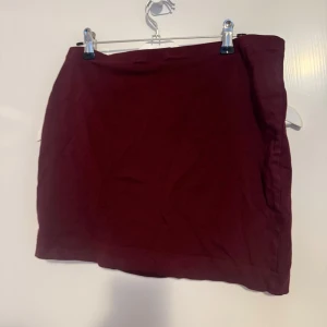 Vinröd kortkjol - Enkel och stilren vinröd kortkjol i mjukt tyg. Kjolen har en rak passform och är i bra skick. 