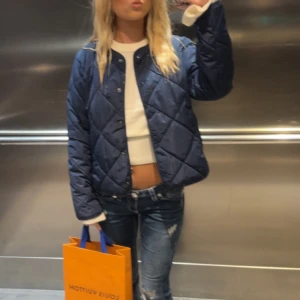 Mörkblå quiltad jacka - Säljer en mörkblå quiltad jacka med tryckknappar framtill från Nelly, perfekt till våren 