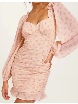 Klänning  - Super fin kort rosa klänning med långa ärmar och blommor och dragkedja i bak från Nelly i storlek 34/xs