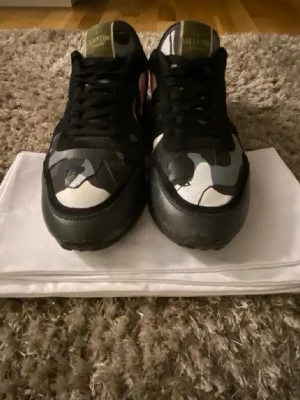 Valentino Rockrunner sneakers camo - Säljer ett par Valentino Rockrunner sneakers med svart, grått, vitt och rosa camouflage-mönster. Skorna har svarta snören, rund tå och detaljer i skinn och textil. Klassisk Valentino-logga på plösen och cool streetwear-vibe.