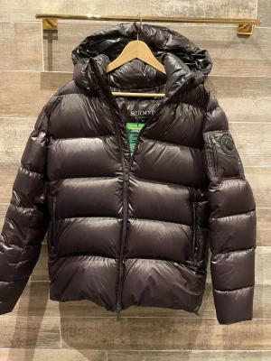 Snoot jacka ny - Säljer en svart pufferjacka från Snoot Stockholm i storlek M. Jackan har huva, dragkedja framtill och en extra ficka med dragkedja på ärmen. Fylld med dun och har en clean, glansig finish. Perfekt för kalla dagar och riktigt snygg streetstil. Nypris 6000