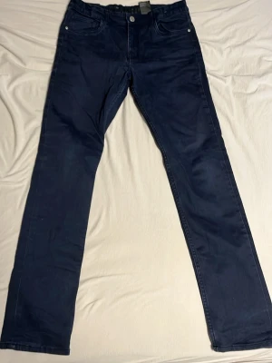 Mörkblå slim fit jeans från H&M - Snygga mörkblå slim fit jeans från H&M i storlek 164. Klassisk femficksmodell med justerbar midja och dragkedja med knapp. Jeansen är tillverkade i bomull med lite stretch för extra komfort. Perfekta till en avslappnad stil.
