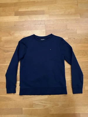 Mörkblå sweatshirt Tommy Hilfiger - Klassisk mörkblå sweatshirt från Tommy Hilfiger med rund halsringning och diskret logga broderad på bröstet. Tröjan har långa ärmar och ribbade muddar vid ärmslut och nederkant. Perfekt till chill vardagsstil.