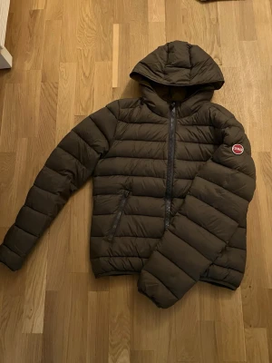 Mörkbrun pufferjacka från Colmar - Säljer en mörkbrun pufferjacka från Colmar med huva och dragkedja framtill. Jackan har två sidofickor med dragkedja och ett broderat Colmar-märke på ärmen. Perfekt för kalla dagar och riktigt skön att bära. Bara använd få gånger