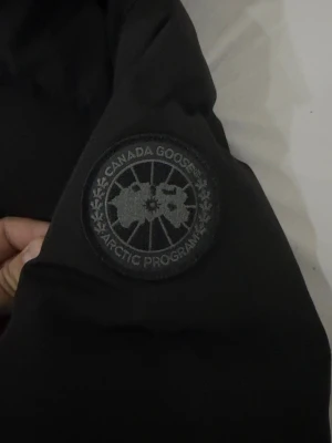 Canada Goose Wyndham Parka - Säljer en svart jacka från Canada Goose. Står XXL men passar L. Jackan har huva, diskret logga på ärmen och dragkedja med knappar. Perfekt för kalla dagar och riktigt snygg streetstil.