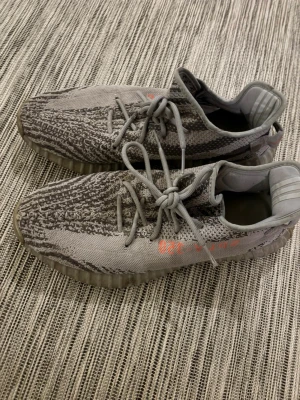 Adidas Yeezy Boost 350 V2 Zebra äkta! - Säljer ett par Äkta Adidas Yeezy Boost 350 V2 Zebra med grått och svart zebramönster, orange text på sidan och genomskinlig ribbad sula. Ovandelen är i stickad syntet och skorna har snörning. Riktigt ikoniska sneakers för dig som gillar streetwear.