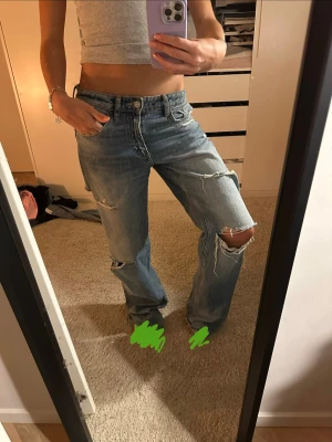 Blå slitna baggy jeans - Säljer ett par ljusblå jeans med flera slitningar och hål på benen för en riktigt avslappnad vibe. Modellen är straight fit med normal midja och klassiska fem fickor. Jeansen är gjorda i bomull och har en vintage tvättad look. Rak modell med lite vidare ben och klassisk passform. Använda men i bra skick, slitningarna är en del av designen. Sköna och enkla att styla till både vardag och fest. 