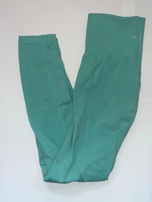 Turkosa träningstights med hög midja - Snygga turkosa träningstights från NVGTN med hög midja och tight passform. Perfekta för träning eller chill, tillverkade i ett stretchigt syntetmaterial som sitter skönt och formar sig efter kroppen.