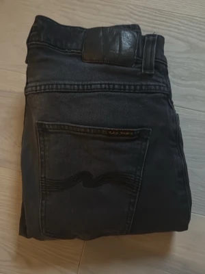  Grim Tim Nudie Jeans - Säljer ett par svarta jeans från Nudie Jeans, modell grim tim som sitter slim på benen. Modellen på bilden är c.a 180cm och på honom sitter jeansen slim och bra i längd! Storleken är W30 L32. Hör av er vid minsta fundering!
