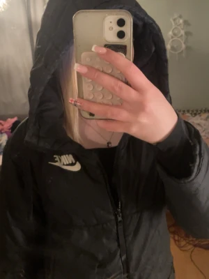 Svart pufferjacka från Nike - Säljer en svart pufferjacka från Nike med huva och dragkedja framtill. Jackan har en clean look med Nike-logga på bröstet och är perfekt för våren. Passar dig som gillar sportig och enkel stil.