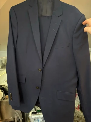 Mörkblå kostym med klassisk passform, Tiger of Sweden - Snygg mörkblå kostym med två knappar framtill och klassiska fickor. Kavajen har smala slag och är helfodrad, perfekt för en stilren look. Långärmad modell med knappar vid ärmslutet. 