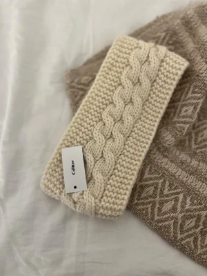 Stickat pannband  - Mysigt stickat pannband i ljusbeige/vit från Glitter. Perfekt accessoar för kyliga dagar. Säljer, då den aldrig kommit till användning. 