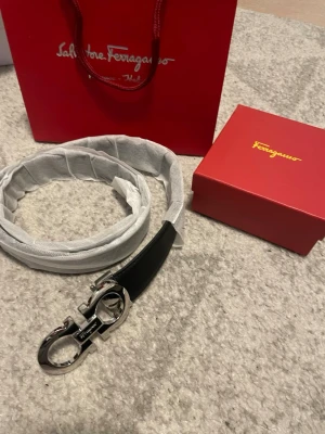 Svart skinnbälte från Salvatore Ferragamo - Säljer ett stilrent svart bälte från Salvatore Ferragamo med exklusivt silverfärgat spänne i metall. Bältet är gjort i slätt skinn och har en klassisk design som passar till både jeans och kostym. Kommer med originalförpackning och dustbag.