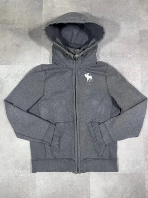 vintage zip-up cardigan från Abercrombie & Fitch - Säljer en vintage zip-up cardigan från Abercrombie & Fitch i snygg grå färg. 🧵 Märke: Abercrombie & Fitch 👕 Storlek: L 🎨 Färg: Grå 📌 Design: Zip-up cardigan 📍 Skick: Mycket bra, se bilder!  Beskrivning: • Tidlös design från Abercrombie & Fitch • Zip-up modell – lätt att ta på och av • Bekväm och mjuk – perfekt för lager-på-lager • Inga fläckar, noppor eller skador (kontrollera bilder) • Lätt att matcha med jeans, chinos eller leggings
