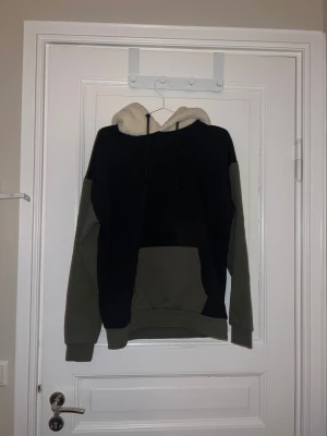 Svart och grön hoodie från Denim Day - Mysig hoodie från Denim Day i svart och grön med fluffig vit luva. Snörning vid luvan och långa ärmar.