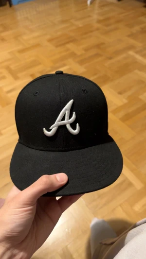 Svart New Era 59FIFTY Atlanta Braves keps - Säljer en svart New Era 59FIFTY keps med Atlanta Braves A-logga broderad i vitt framtill. Klassisk flat brim och MLB-logga bak. Den är i bra skick och storlek 7 (55.8cm)