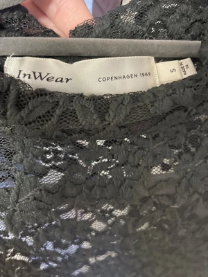 Svart spetsblus från InWear - Säljer en svart långärmad blus från InWear i storlek S. Blusen är helt i spets med ett blommigt mönster och har en hög hals. Perfekt för dig som gillar detaljer och vill ha en elegant look med transparent känsla.