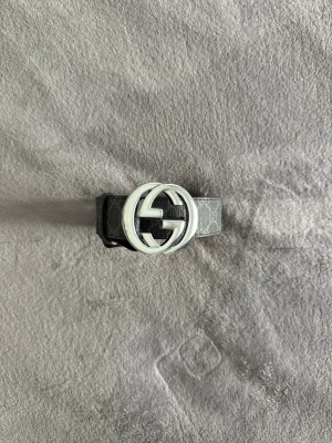 Gucci bälte  - Säljer ett svart Gucci-bälte med klassiskt GG-mönster och en stor, rund silverfärgad GG-logga som spänne. Bältet är tillverkat i äkta skinn och har en lyxig känsla med snygga detaljer. Perfekt för dig som vill ha en statement-accessoar från ett ikoniskt märke.