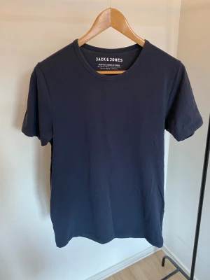 Mörkblå t-shirt från Jack & Jones -storlek Medium  - Snygg mörkblå t-shirt från Jack & Jones med klassisk rund hals och korta ärmar. Tillverkad i mjuk bomull med lite elastik för komfort. Enkel och stilren design utan mönster eller tryck, perfekt för en chill och avslappnad look.