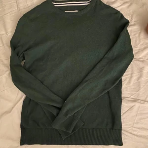 Grön tröja med rund hals - Säljer en stilren grön tröja med rund hals och ribbade muddar. Perfekt för kyligare dagar. Tröjan har långa ärmar och är tillverkad i ett mjukt material.